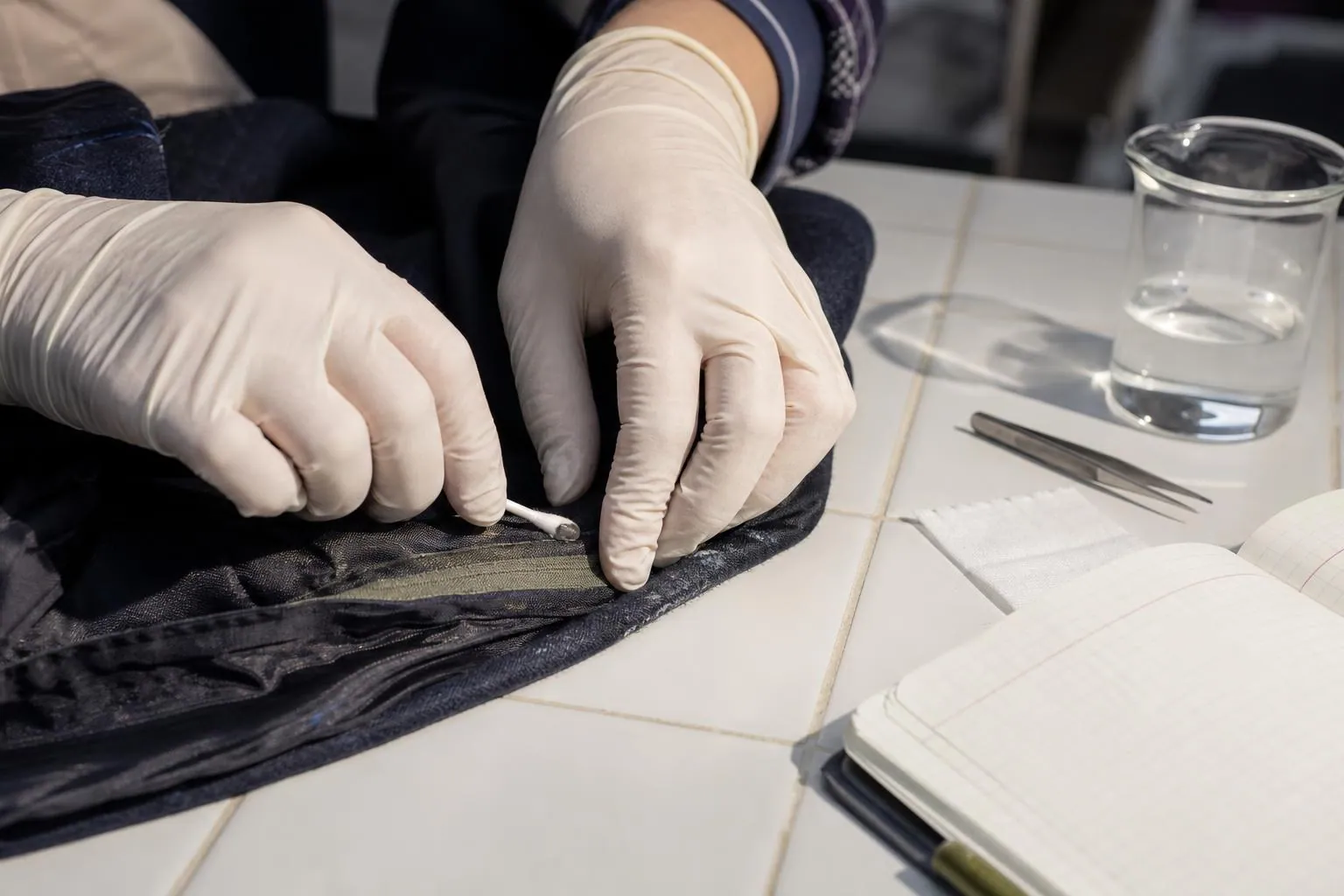 Mains gantées frottant un coton tige sur la réserve de couture intérieure d’une veste pour tester la solidité de la couleur